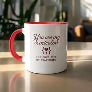 Op de afbeelding: Witte keramische mok met een rode binnenkant en handvat. De mok heeft de tekst "You are my semicolon" met een hartsymbool en de zin "YOU COMPLETE MY STATEMENT" in bruine letters.