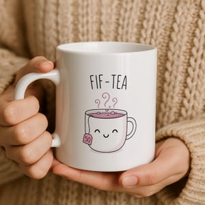 Mug with "FIF-TEA" text and smiling tea bag graphic.