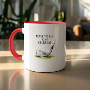 White mug with red handle, featuring golf club, ball, and text "Never too old to go clubbing".