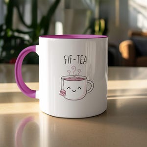 White mug with purple handle and "FIF-TEA" text and smiling teabag.