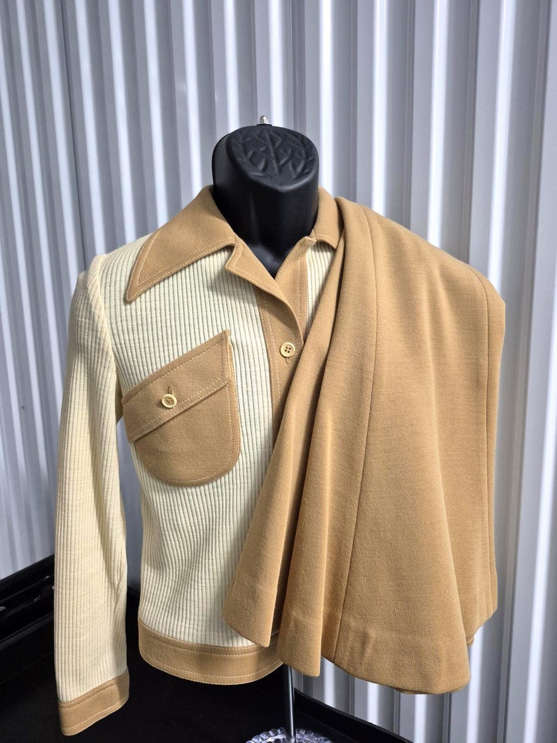 A vintage two-piece suit in cream and caramel tan. The jacket has a ribbed cream front with a tan collar, pocket, and button details. The matching skirt is a solid tan color. The suit is displayed on a mannequin. Size 8, By Act III, a vintage company of Jonathan Logan.