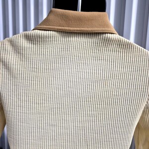 Another back view, Close-up of a cream-colored ribbed shirt with a tan collar. The shirt is hanging on a black hanger mannequin. The ribbed texture runs vertically down the shirt. The collar is a solid tan color.