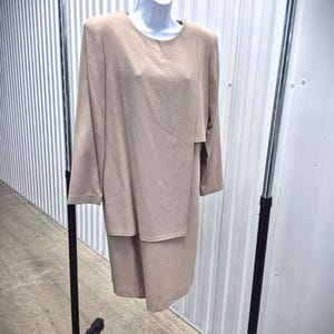 May include: A beige two-piece dress set displayed on a clothing rack. The set includes a long-sleeved top with a layered design and a matching knee-length skirt. The dress is made of a textured fabric.