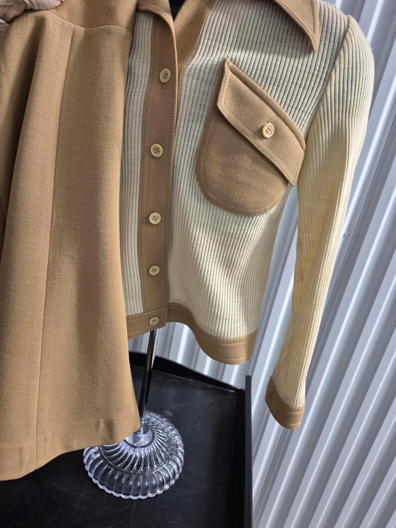 A vintage two-piece outfit in cream and tan. The top is a cream button-down shirt jacket style with contrasting tan pocket and a wide 60s collar. The skirt is a solid tan color. The outfit is displayed on a mannequin.