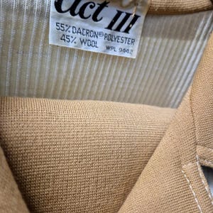 Close-up of a tan-colored garment with a label that reads "Act III." The label also indicates the fabric composition: 55% Dacron polyester and 45% wool. The garment has a ribbed texture for the top and a double knit skirt.