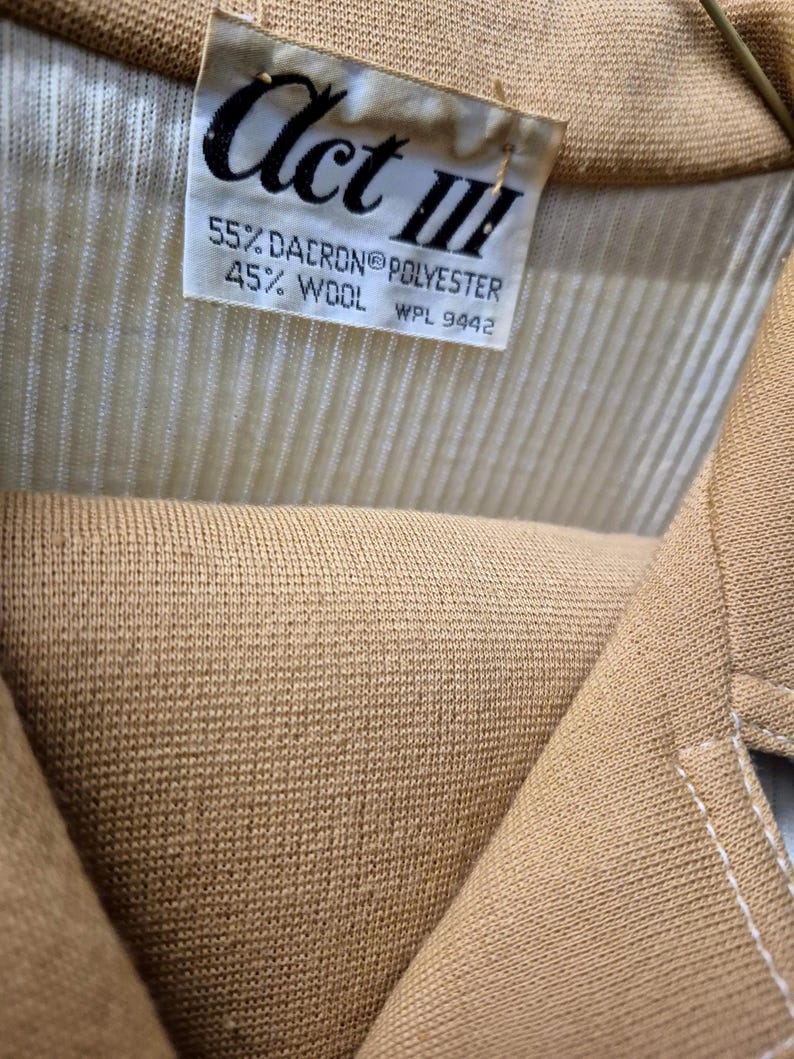 Close-up of a tan-colored garment with a label that reads "Act III." The label also indicates the fabric composition: 55% Dacron polyester and 45% wool. The garment has a ribbed texture for the top and a double knit skirt.