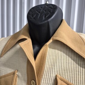 A tan and cream-colored vintage shirt with a wide pointed collared neckline and two front pockets. The shirt features a ribbed knit material on the body and contrasting solid tan double knit fabric accents on the collar, pockets, and button placket.