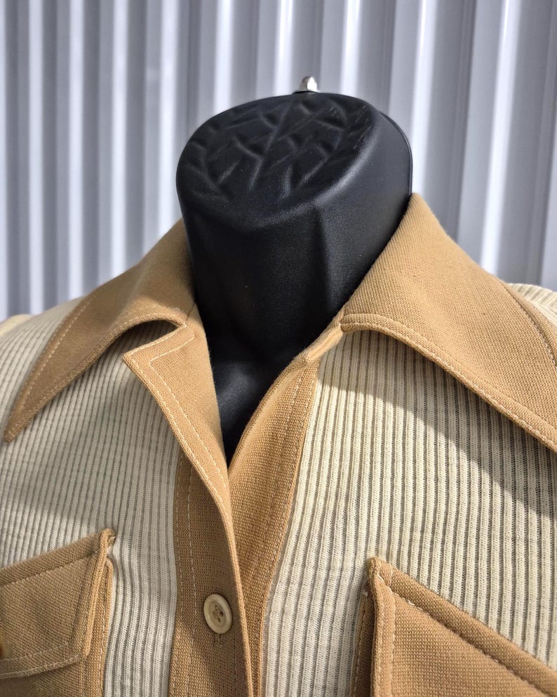 A tan and cream-colored vintage shirt with a wide pointed collared neckline and two front pockets. The shirt features a ribbed knit material on the body and contrasting solid tan double knit fabric accents on the collar, pockets, and button placket.