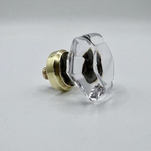 May include: Clear faceted glass door knob with a brass base. The knob has a geometric design and is mounted on a brass base. The glass is transparent, allowing light to pass through. A classic hardware element.