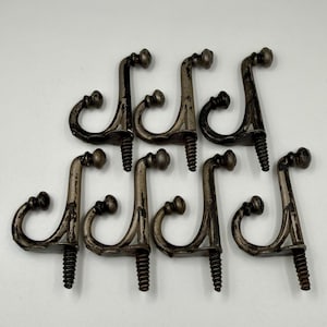 May include: Eight antique-style metal hooks with a tarnished silver finish. Each hook has a curved design with a decorative ball at the top and a threaded screw for mounting. The hooks are arranged against a white background.