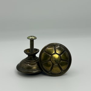 Puede incluir: Dos tiradores de armario antiguos de latón. Uno es redondo con un diseño floral, y el otro tiene un tornillo adjunto. Los tiradores tienen un aspecto deslustrado y envejecido, lo que sugiere que son vintage o de inspiración vintage.