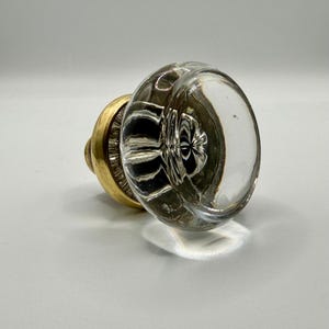 May include: A clear glass doorknob with a ribbed interior and a brass base. The knob is round and reflects light, creating a bright, clean appearance. The brass base has a circular design.