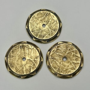 May include: Three antique brass-colored metal discs with a textured, crumpled surface and a central hole. The edges have a decorative, wavy border. These decorative elements could be used for crafts or home decor.