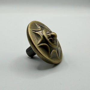 Op de afbeelding: Antieke messing kastknop met een zonneradiatie-ontwerp. De ronde knop heeft een verhoogd zonachtig patroon en een donkere, cilindrische steel. Ideaal voor meubelrestauratie of een vintage touch. Diameter ongeveer 4 cm.