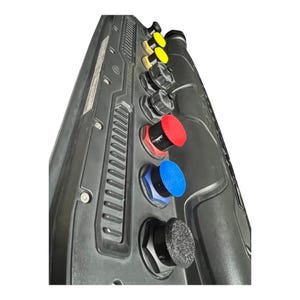 May include: A black control panel with several colored buttons. The buttons are red, blue, yellow, and black. The panel has a textured surface and various mechanical components.