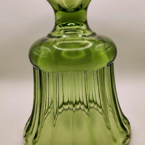 May include: A green glass decorative piece with a flared base and a ruffled top. The glass has vertical ridges and a bulbous midsection. The piece is likely vintage and adds a touch of elegance.
