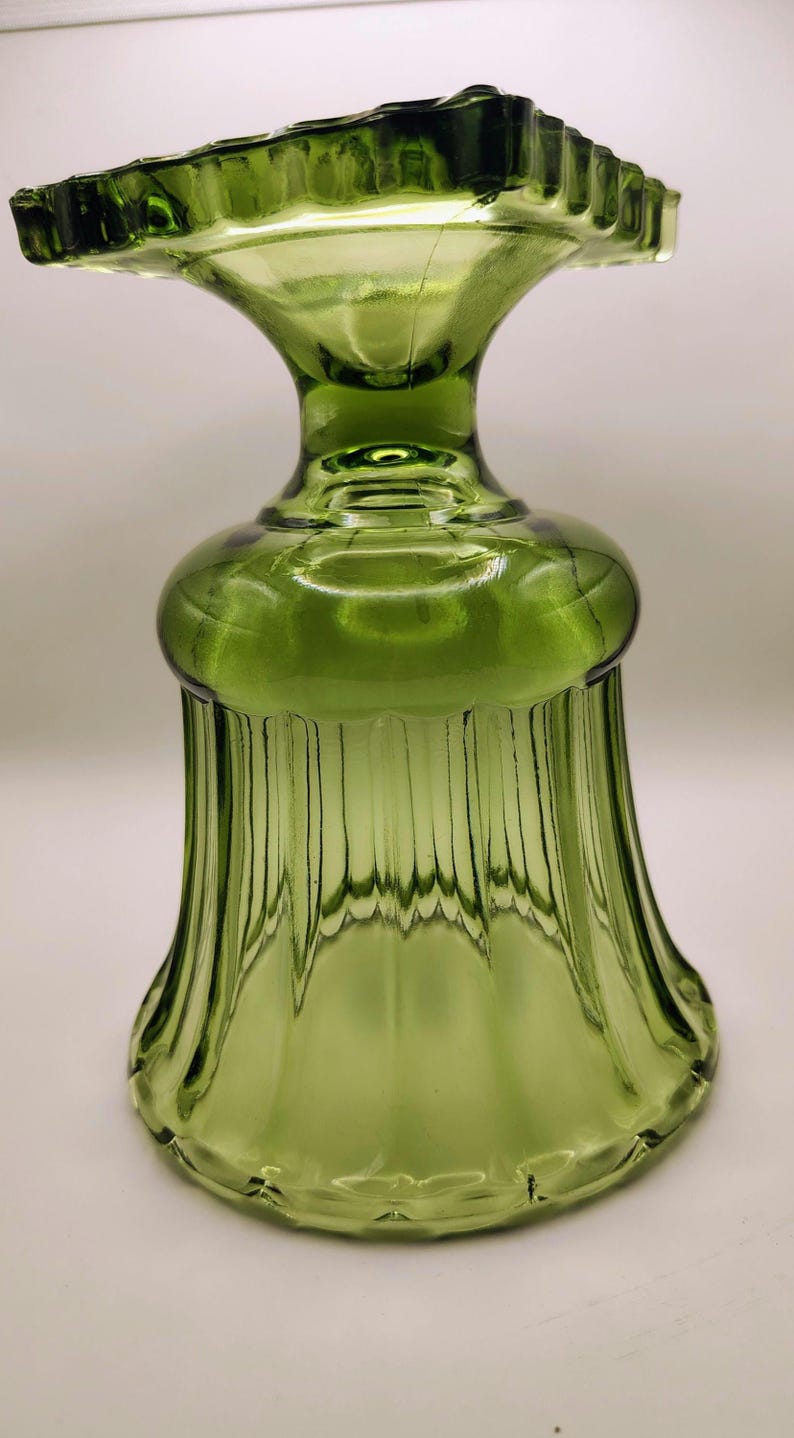 May include: A green glass decorative piece with a flared base and a ruffled top. The glass has vertical ridges and a bulbous midsection. The piece is likely vintage and adds a touch of elegance.