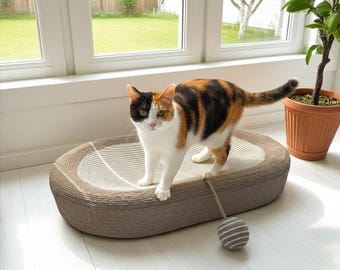 May include: A calico cat stands on a brown and beige cat scratcher with a dangling toy. The cat has a white chest and paws, with patches of black, orange, and brown fur. The scratcher is oval-shaped and sits on a white floor.