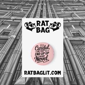 Könnte beinhalten: Ein rosa Button mit dem Text "Careful, or you'll end up in my novel" und einer Bleistift- und Buchgrafik. Der Button ist Teil eines Designs, das ein Logo mit einer Sonnenbrille tragenden Maus und den Worten "RAT BAG" enthält.