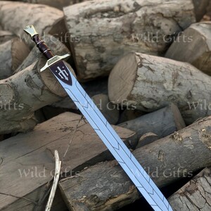 May include: A silver-colored sword with a brown handle and gold accents. The blade has a decorative design. The sword is resting on a pile of wooden logs. The text "Wild Gifts" is visible in the background.