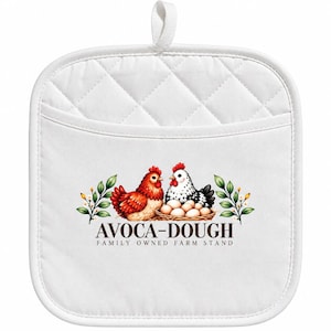May include: A white quilted pot holder with a hanging loop. The centre features a graphic of a red hen and a speckled white hen sitting by a nest of eggs, flanked by green leaves. Below the graphic is the text AVOCA-DOUGH FAMILY OWNED FARM STAND.