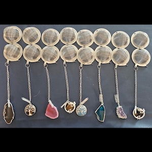 May include: A collection of tea infusers with silver chains and decorative charms. The charms include various gemstones, a tree of life, and other designs. The infusers are made of a fine mesh material.