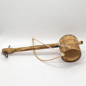 May include: A handmade wooden musical instrument with a cylindrical body and a long, thin neck. The instrument has detailed carvings and a string stretched across the neck. The text "ImaniKrafts" is visible on the side.