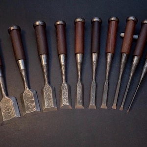 Könnte beinhalten: Eine Sammlung von neun Holzmeißeln mit dunkelbraunen Holzgriffen und silberfarbenen Klingen. Die Meißel sind in einer Reihe angeordnet und zeigen ihre unterschiedlichen Klingenformen und -größen. Die Griffe haben eine Metallkappe.