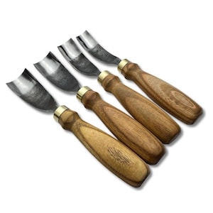 Może przedstawiać: Zestaw pięciu dłut do rzeźbienia w drewnie. Każde dłuto ma zakrzywione, srebrne ostrze, mosiężną tuleję i drewniany uchwyt. Uchwyty mają naturalne usłojenie drewna. Narzędzia są ułożone po przekątnej na białym tle.