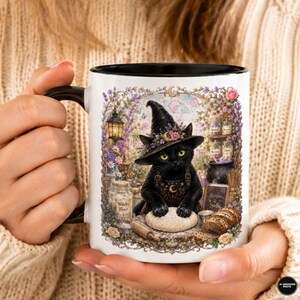 May include: A white ceramic mug with a black handle and interior, featuring a detailed illustration of a black cat wearing a witch hat and overalls, kneading dough in a magical kitchen setting filled with jars, flowers, and a lantern.