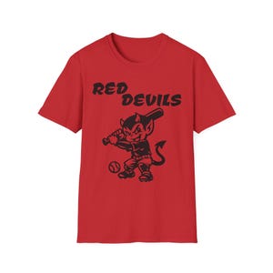 May include: Red t-shirt with a black graphic of a devil character holding a baseball bat, with a baseball at its feet. The text "RED DEVILS" is arched above the character. The shirt is made of a soft material.