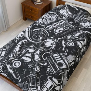 May include: Black and white comforter featuring a detailed pattern of automotive engine components. The design includes pistons, gears, and other mechanical parts, creating a bold, graphic aesthetic. The comforter is on a wooden bed frame.