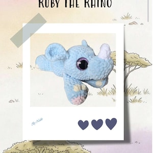 Könnte beinhalten: Ein hellblaues gehäkeltes Nashorn-Stofftier mit einem weißen Horn, großen violetten Glitzeraugen und hellrosa Akzenten an den Füßen. Das Bild enthält den Text Ruby The Rhino, By Nekko und drei dunkelblaue Herzsymbole in einem Polaroidrahmen.