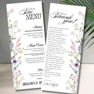 Könnte beinhalten: Zwei elegante Hochzeitsmenükarten mit floralen Akzenten. Die linke Karte trägt die Aufschrift "The Menu" und listet Vorspeisen und Hauptgerichte auf. Die rechte Karte sagt "Thank you!" und enthält eine Dankesbotschaft. Die Karten haben ein zartes Blumendesign.
