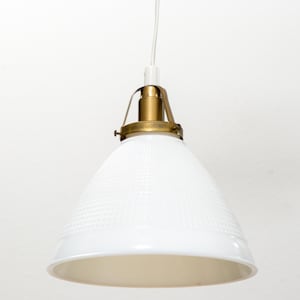 May include: A white pendant light fixture featuring a conical shade with a subtle textured grid pattern. The shade is attached to a brass-toned metal hardware assembly at the top, which connects to a thin white electrical cord for ceiling suspension.