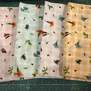 May include: Five fabric swatches with floral patterns. The fabrics are in shades of green, pink, blue, white, and yellow. Each swatch features a different floral design with small flowers and leaves scattered across the surface.