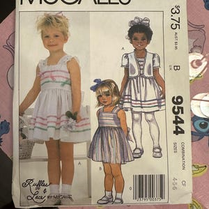 May include: A vintage McCall's sewing pattern for girls' dresses. The pattern features illustrations of children's dresses with striped and ruffled details. The pattern includes sizes 4-5-6 and the text "Ruffles & Lace for McCall's".