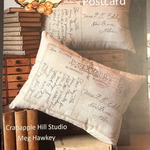 May include: Two rectangular throw pillows with a vintage postcard design. The pillows are beige with handwritten text and a postal stamp. The image also includes books and the text "Crabapple Hill Studio".