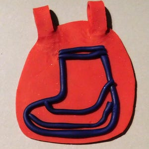 Könnte beinhalten: Eine rote, abgerundete Form mit zwei kleinen, erhöhten Schlaufen oben. Eine blaue Stiefelkontur ist auf der roten Form zentriert. Das Stiefeldesign besteht aus einer dicken, gebogenen Linie.