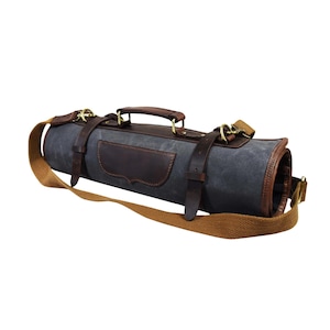 Könnte beinhalten: Eine aufgerollte graue Messerrolle aus Canvas mit braunen Lederakzenten, Riemen und Griff. Die Tasche hat einen braunen Schultergurt und goldfarbene Metallbeschläge. Der Lederaufnäher auf der Vorderseite verleiht diesem Küchenzubehör einen Hauch von Eleganz.