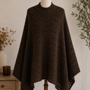 Peut inclure: Un poncho tricoté marron foncé avec un col montant et un motif ajouré décoratif. Le poncho est présenté sur un mannequin, mettant en valeur son design fluide et asymétrique. Le vêtement est fait d'une matière douce et texturée.