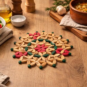 Puede incluir: Un salvamanteles de madera con diseño floral, con madera natural, detalles rojos y verdes. Se encuentra sobre una mesa de madera, junto a cuencos de comida, aceite y especias, sugiriendo un ambiente de cocina o comedor. Aproximadamente 20 cm de diámetro.