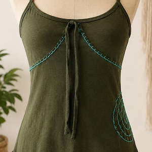 May include: Olive green tank top with thin straps and a scoop neckline. The top features teal stitching along the neckline and hem, with a spiral design on the side. A tie detail is at the center of the neckline.