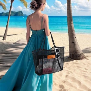 以下が含まれることがあります： 長めのティール色のドレスを着た人が、黒いメッシュのトートバッグと白いサングラスを持っています。砂浜にはヤシの木と青い海が広がっています。バッグには長方形の革のタグが付いています。