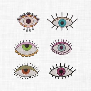 Puede incluir: Seis diseños de ojos bordados en varios colores, incluyendo rosa, azul, verde y naranja, con contornos negros. Cada ojo tiene un estilo único, algunos con pestañas y elementos decorativos.