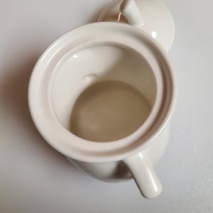 May include: Cream-colored ceramic sugar bowl with a matching lid. The bowl has a rounded body, a small handle, and a wide opening. The lid has a small knob for easy removal. The sugar bowl is set against a white background.