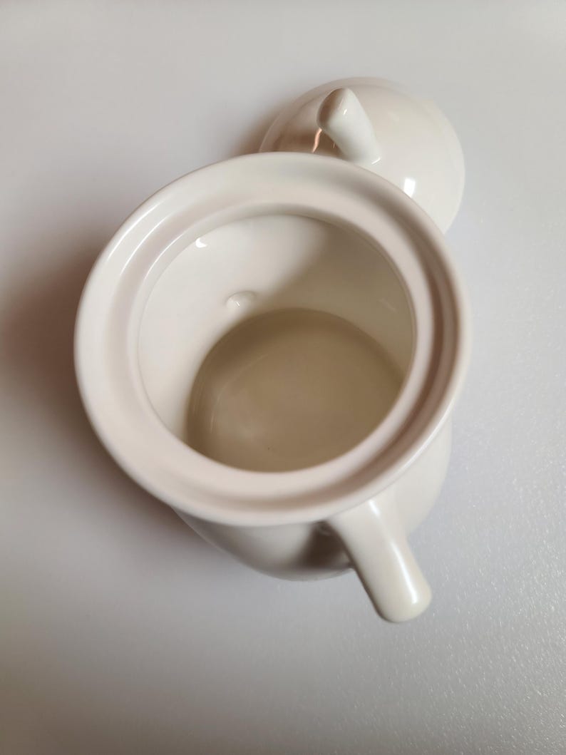 May include: Cream-colored ceramic sugar bowl with a matching lid. The bowl has a rounded body, a small handle, and a wide opening. The lid has a small knob for easy removal. The sugar bowl is set against a white background.