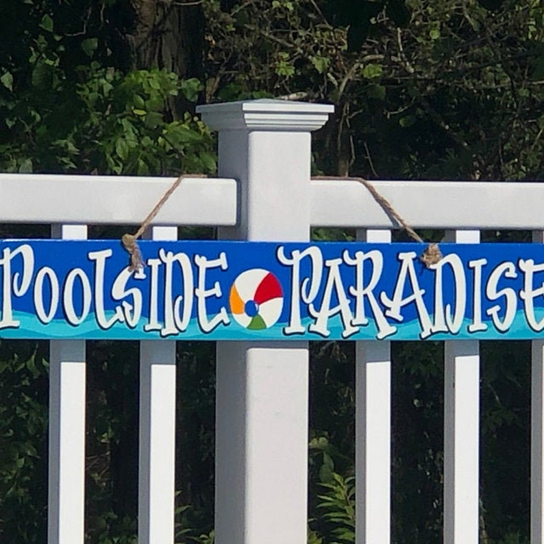 May include: A blue and white wooden sign with the text "Poolside Paradise" and a colourful beach ball graphic.