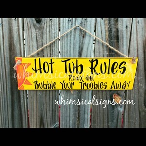 May include: A yellow wooden sign with the words "Hot Tub Rules" in black script, along with "Relax and Bubble Your Troubles Away." A sun graphic is in the upper left corner. The sign hangs from a twine string.