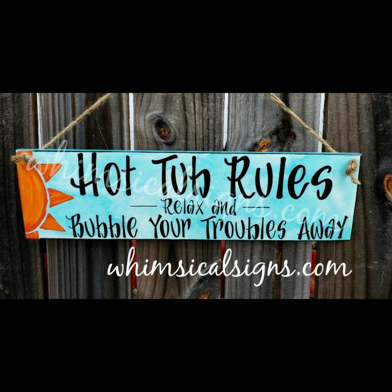 May include: A rectangular wooden sign with the text "Hot Tub Rules" and "Bubble Your Troubles Away" in black lettering. The sign has a light blue background with an orange sun graphic. It hangs by a natural twine.